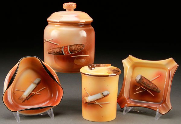 4 PIECE NORITAKE PORCELAIN SMOKING SET: A FOUR PIECE HAND PAINTED NORITAKE PORCELAIN SMOKING SET, EARLY 20TH CENTURY. Decorated with cigar and cigarette motifs, comprising a humidor, a cigarette jar, and two ash trays. All with green "M in