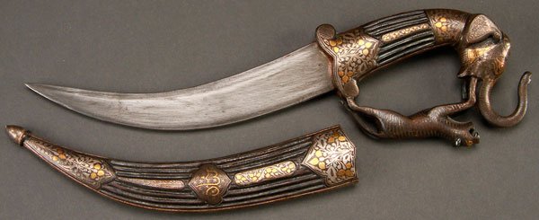 ORNATE INDO-PERSIAN DAGGER: ORNATE INDO-PERSIAN DAGGER. The curved blade with inlaid floral cartouche and the handle with elephant pommel and tiger hand guard in silver and gold niello. The fluted scabbard also with silver and