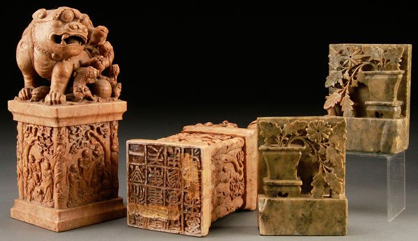 A FOUR PIECE CHINESE CARVED SOAP STONE GROUP: A FOUR PIECE CHINESE CARVED SOAP STONE GROUP, 20TH CENTURY. Comprising a large pair of figural carved seals modeled as Foo dogs with young, surmounting a scenic paneled plinth with immortals, the base