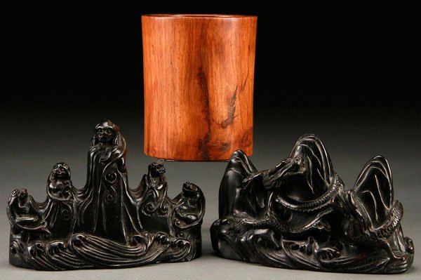 A PAIR OF CHINESE CARVED EBONY ORNAMENTS: A PAIR OF CHINESE CARVED EBONY ORNAMENTS. Finely carved with Qilin and dragons on rockery ground rising above stylized waves. Together with a Jichimu wood brush pot. Largest height 6.25 inches (16 cm)