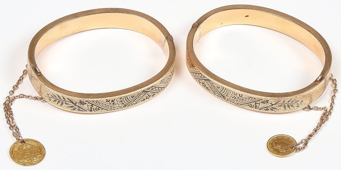 PAIR OF 14K GOLD BRACLETS AND COINS: PAIR OF 14K GOLD BRACLETS AND COINS. Comprising a pair of matching 14k yellow gold bracelets with ornate engraved vines and designs with niello accents. Each with a gold coin charm suspended by a chai