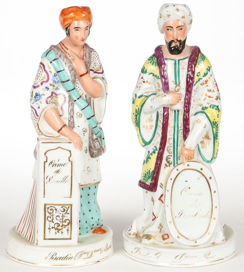 FRENCH PORCELAIN BADIN DECANTERS 19TH C: FRENCH PORCELAIN BADIN DECANTERS 19TH C. Comprising a pair of matching porcelain figures depicting a sultan with shield and his wife, each inscribed in gold with a particular liqueur and with French g