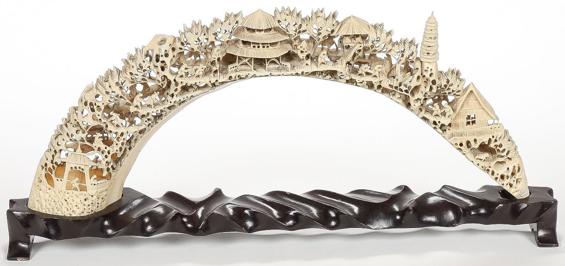 CHINESE CARVED TUSK VILLAGE: CHINESE CARVED TUSK VILLAGE. Comprising an ornate and finely pierced carved village scene with various figures, buildings and fauna resting on a conforming wood stand. Height on stand 7 inches (17.5cm