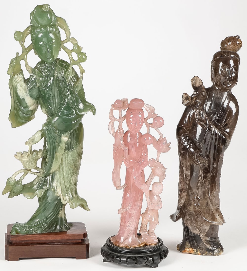 CHINESE CARVED JADE AND QUARTZ FIGURES: CHINESE CARVED JADE AND QUARTZ FIGURES. Comprising three carved figures of Guanyin, one in smoky quartz, one in pink quartz, and one in green jade (repaired). Greatest height 17 inches (43.5cm).SHIPP