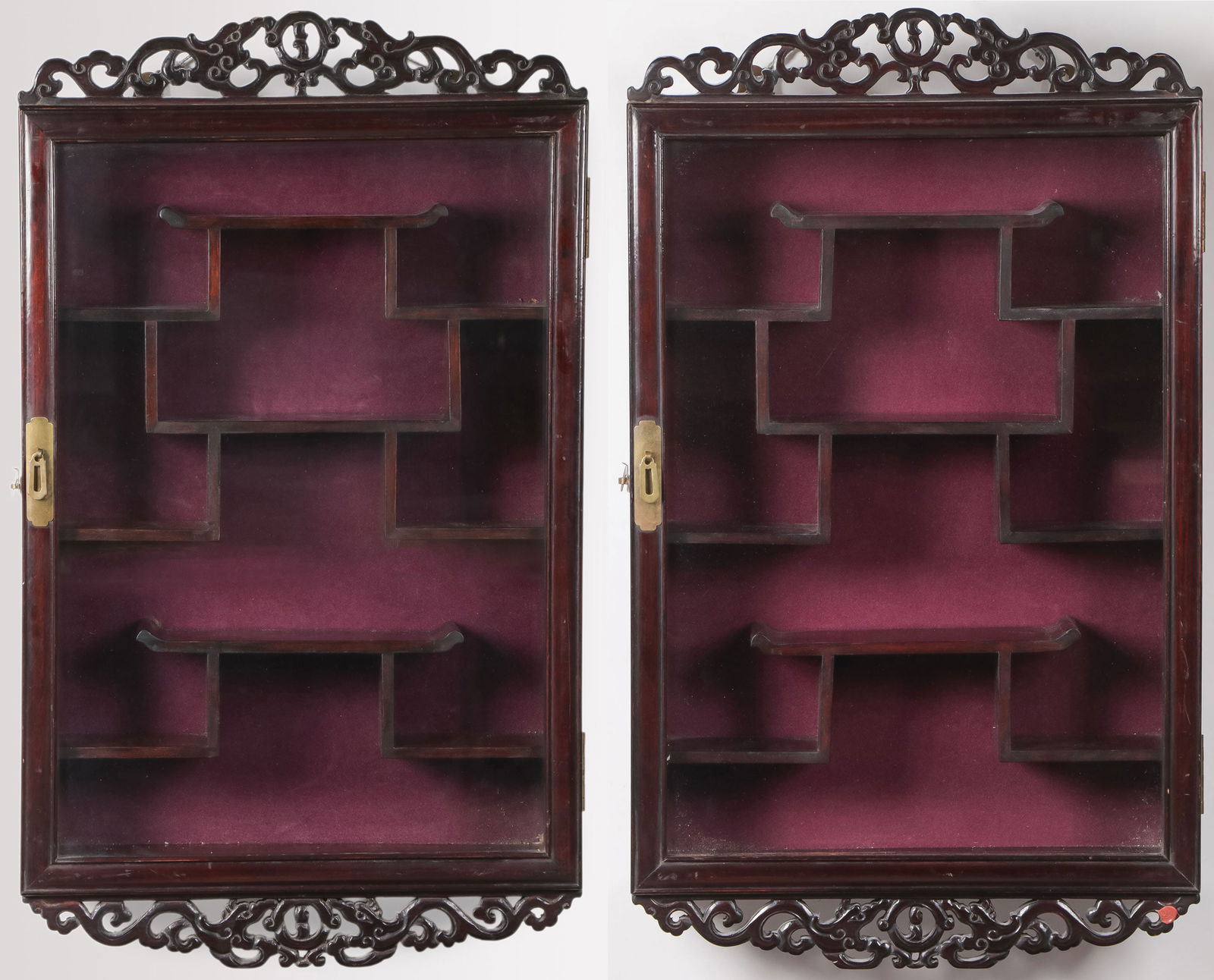 PR MATCHING CHINESE CURIO CABINETS: PR MATCHING CHINESE CURIO CABINETS. Comprising a pair of matching Chinese carved wood wall-mounted curio cabinets. Each with pierced-carved crest and skirt, the interior with similarly configured shel