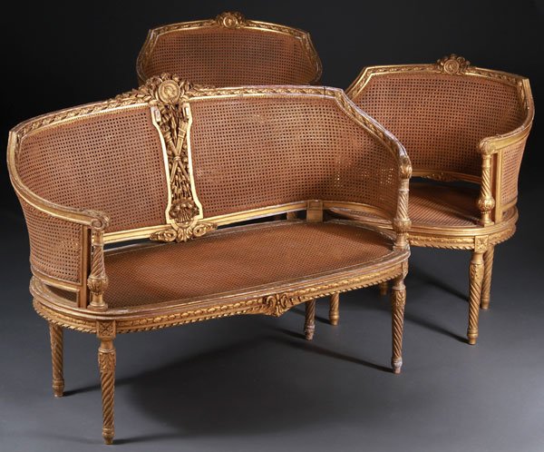 FRENCH CARVED AND GILT WOOD 3 PIECE PARLOR SET: A FRENCH LOUIS XVI STYLE CARVED AND GILT WOOD THREE PIECE PARLOR SET, 19TH CENTURY. Comprising a barrel form settee with caned back and seat within a foliate carved framework centered with an openwork