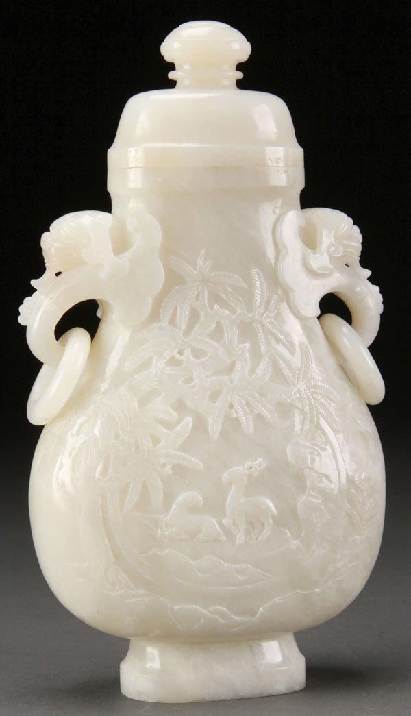 A CHINESE CARVED WHITE JADE LIDDED URN: A CHINESE CARVED WHITE JADE LIDDED URN. Of flattened ovoid form with figural mythical beast handles suspending loose rings above a relief carved scene of deer and bats. The verso with calligraphy insc