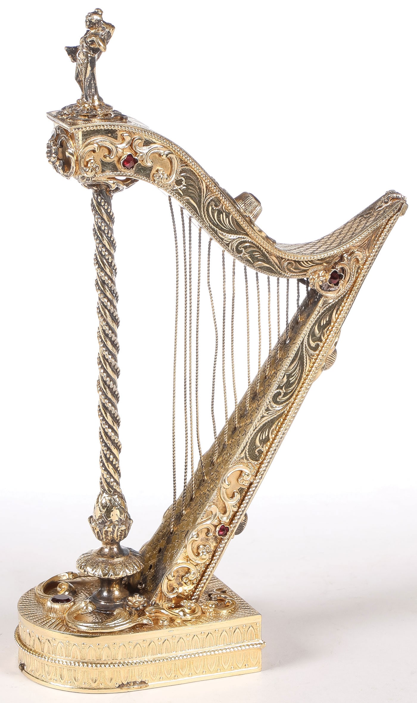 ORNATE SILVER-GILT AND JEWELED HARP: ORNATE SILVER-GILT AND JEWELED HARP. Comprising an ornate continental silver-gilt harp with applied rocaille scrolls and overall chased and set with a cut red gemstone and with figural finial.