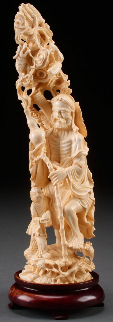 A LARGE CHINESE CARVED IVORY FIGURE OF AN IMMORTAL: A LARGE CHINESE CARVED IVORY FIGURE OF AN IMMORTAL, 20TH CENTURY. With staff and attendant at feet holding a vase with flowing cloud forms containing various Buddhist symbols. Total height 13.5 inches