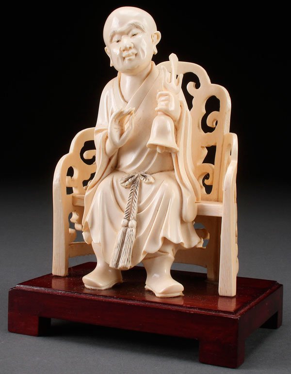 A FINE CHINESE CARVED IVORY BUDDHIST FIGURE: A FINE CHINESE CARVED IVORY BUDDHIST FIGURE, 20TH CENTURY. Depicted seated on a scroll carved armchair holding a bell and raised on a wooden stand. Inscribed reign mark on verso. The ivory 6.25 inches