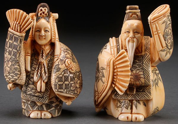 A VERY FINE PAIR OF JAPANESE CARVED IVORY FIGURES: A VERY FINE PAIR OF JAPANESE CARVED IVORY FIGURES, 20TH CENTURY. In the form of elaborately dressed entertainers with fans, displayed on a scroll form hardwood stand. The ivory height 3.5 inches (8 cm