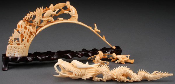 A PAIR OF CHINESE CARVED IVORY FIGURES: A PAIR OF CHINESE CARVED IVORY FIGURES, 20TH CENTURY. Comprising a boar tusk with pierced scene of workers and animal forms, and a reticulated scrolling dragon. Each displayed on carved hardwood stand