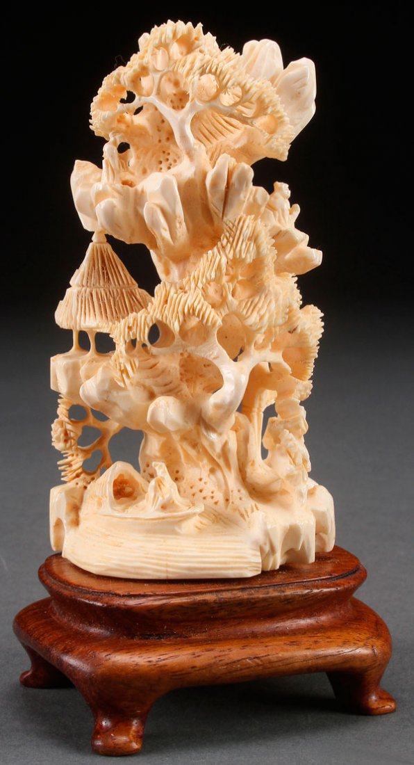 A CHINESE CARVED IVORY MOUNTAINOUS SCENE: A CHINESE CARVED IVORY MOUNTAINOUS SCENE, 20TH CENTURY. With pierced decoration of pavilions, pine trees and immortals, carved in the round. Raised on a footed carved hardwood stand, the ivory height