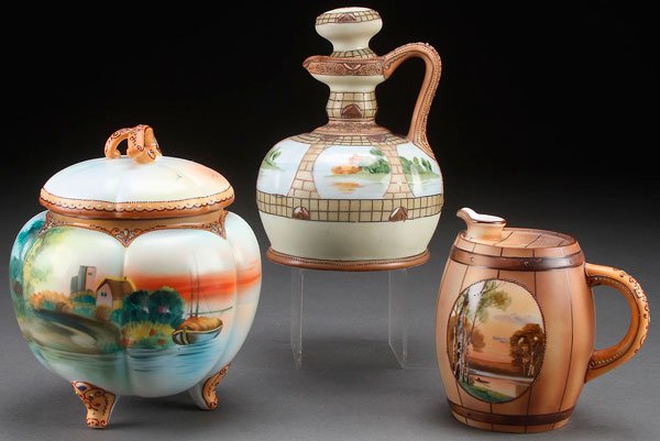 A THREE PIECE GROUP OF HAND PAINTED NIPPON PORCELAIN: A THREE PIECE GROUP OF HAND PAINTED NIPPON PORCELAIN, EARLY 20TH CENTURY. Comprising a whiskey jug in the form of a barrel painted with a scenic design, a wine jug with raised enamel decorated panels 