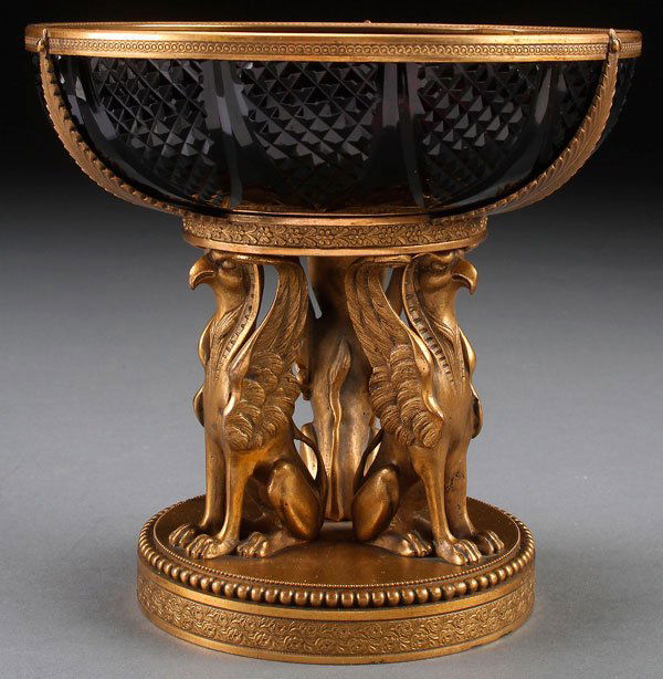 AN AUSTRIAN NEO-CLASSIC GILT BRONZE AND CUT GLASS TAZZA: AN AUSTRIAN NEO-CLASSIC GILT BRONZE AND CUT GLASS TAZZA, CIRCA 1900. The well modeled figural base in the form of three winged griffins on a circular beaded plinth surmounted with an amethyst glass bo