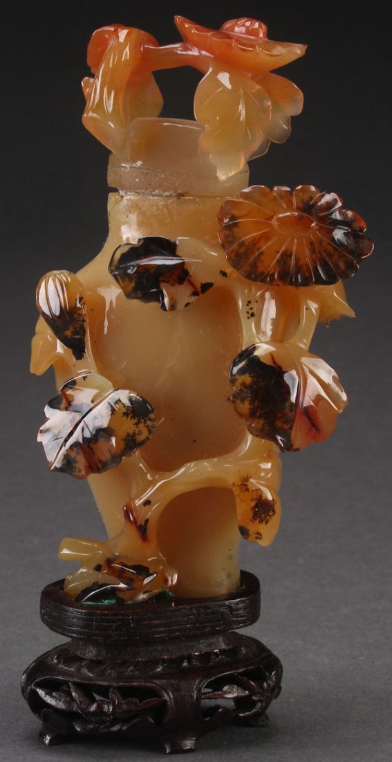 A CHINESE CARVED CARNELIAN AGATE LIDDED URN: A CHINESE CARVED CARNELIAN AGATE LIDDED URN, 20TH CENTURY. With extending floral decoration, raised on a carved wooden stand. Total height 5.5 inches (14 cm).