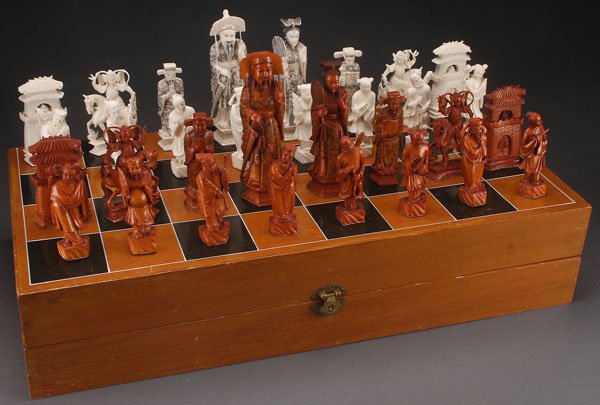 AN ORIENTAL CARVED IVORY CHESS SET: AN ORIENTAL CARVED IVORY CHESS SET. With tea stained and natural colored chess pieces in the form of Chinese figures, contained in a wood chess board game box. Largest piece height 6.75 inches (10 cm