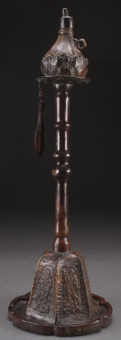 A LARGE KOREAN BRONZE PRICKET FORM OIL LAMP: A LARGE KOREAN BRONZE PRICKET FORM OIL LAMP, 19TH/20TH CENTURY. The lotus form base decorated with Buddhist figures in relief below an elongated double knopped stem with double lotus terminal containi
