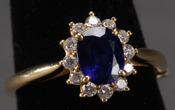 LADIES TIFFANY & CO. 18K BLUE SAPPHIRE , DIAMOND RING: A LADIES TIFFANY & CO. 18K GOLD, BLUE SAPPHIRE AND DIAMOND RING, 20TH CENTURY. Containing an oval cut blue sapphire approximately 6.5 x 5 mm surrounded by 12 round cut diamonds. Size 4 ¾-5, containe