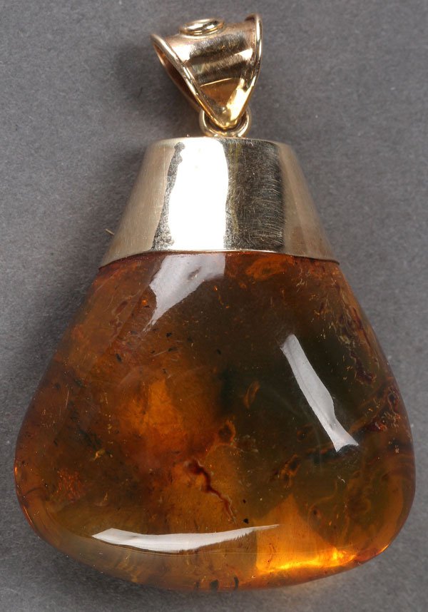 A GOLD MOUNTED DOMINICAN AMBER PENDANT: A GOLD MOUNTED DOMINICAN AMBER PENDANT, OLIGOCENE PERIOD. Of flattened triangular form with wispy dark inclusions. Length 2 inches (51 mm).