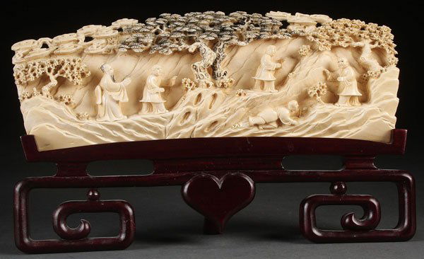 A CHINESE EXPORT CARVED IVORY SCENIC PLAQUE, QING: A CHINESE EXPORT CARVED IVORY SCENIC PLAQUE, QING DYNASTY. Carved in good relief with five figures below pine trees and cloud forms on a rockery ground, the verso carved with a rockery formation. Leng