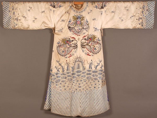 A CHINESE EMBROIDERED SILK WINTER COURT ROBE: A CHINESE EMBROIDERED SILK WOMAN'S INFORMAL WINTER COURT ROBE, 20TH CENTURY. Finely stitched with dragons, gilt threads and Buddhist symbols on a white ground, above a wavy blue border. Width 77 inche