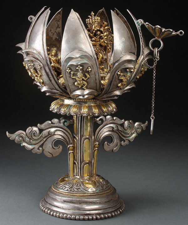 A LARGE TIBETAN SILVER BUDDHIST SHRINE: A LARGE TIBETAN SILVER AND SILVER-GILT ARTICULATING LOTUS FORM BUDDHIST SHRINE, PROBABLY 20TH CENTURY. Modeled as a lotus blossom bud, the exterior with applied gilt deities raised on a winged scrolle