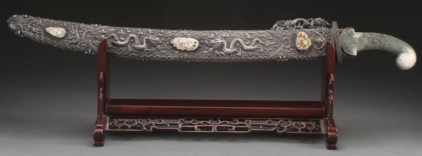 CHINESE JADE AND SILVER CEREMONIAL SWORD: AN IMPRESSIVE CHINESE MONGOLIAN STYLE JADE AND SILVER CEREMONIAL SWORD WITH SHEATH, 20TH CENTURY. The steel blade fitted with an archaic form carved celadon hade handle, contained in a silver overlaid
