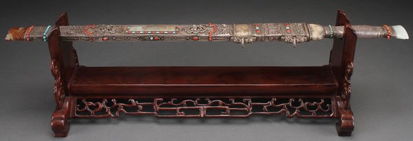 A CHINESE MONGOLIAN STYLE JADE MOUNTED SWORD: A CHINESE MONGOLIAN STYLE JADE MOUNTED SWORD AND SILVER SHEATH, 20TH CENTURY. Of archaic form, the steel double edged blade with silver mounted handle and white jade pommel, carved with a figural bat.