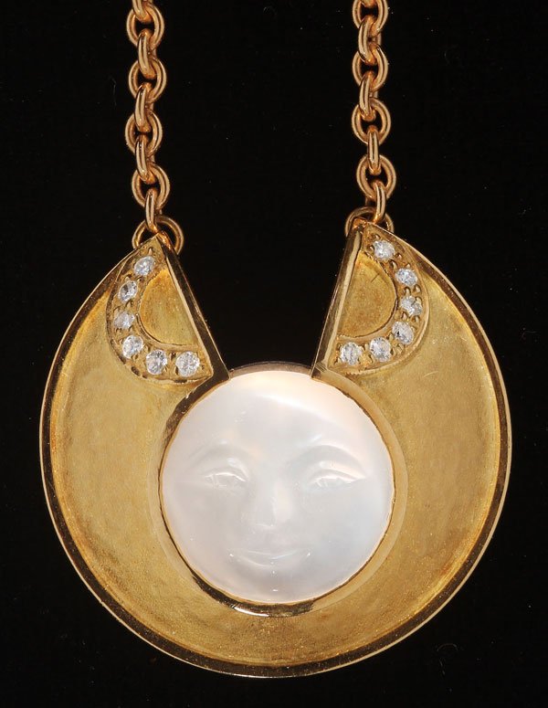18K CARVED MOONSTONE & DIAMOND PENDANT NECKLACE: AN 18K CARVED MOONSTONE AND DIAMOND PENDANT NECKLACE, LATE 20TH CENTURY. The cabochon moonstone approximately 12 mm diameter, carved with a facial form within an 18K gold flared collar set with two pa