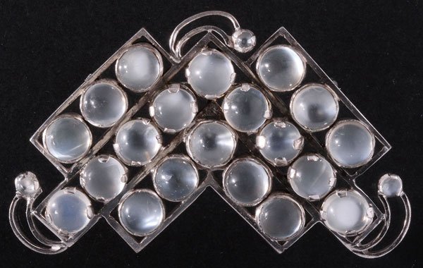AN ART DECO STYLE SILVER AND MOONSTONE BROOCH: AN ART DECO STYLE SILVER AND MOONSTONE BROOCH, LAST HALF 20TH CENTURY. Comprised of angular bars with scrolled terminals each prong set with round cabochon moonstones approximately 7mm diameter, appar
