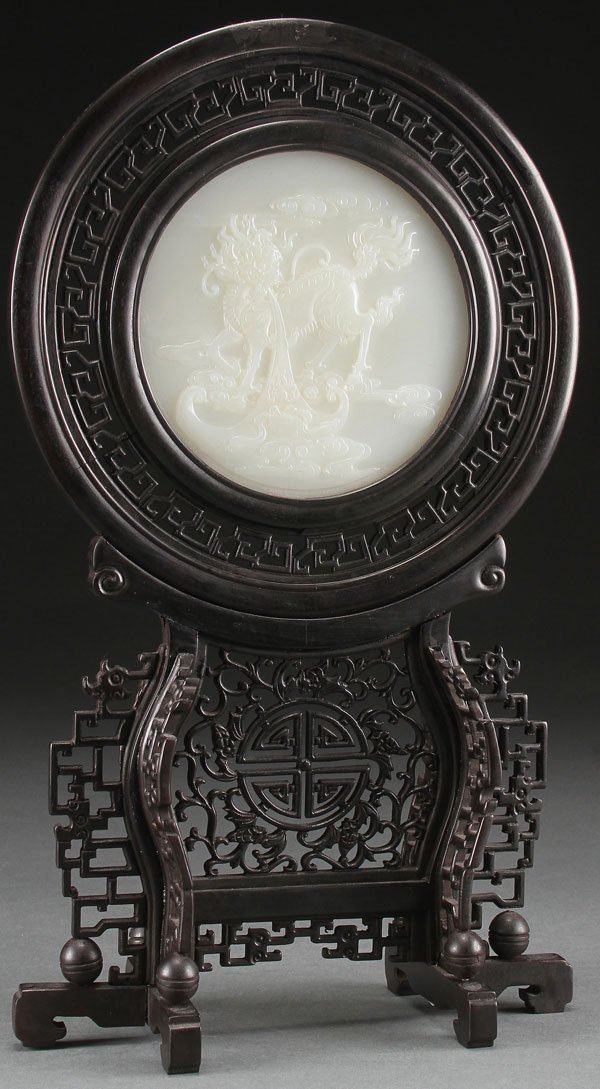 CHINESE CARVED HARDSTONE AND CARVED WOOD TABLE SCREEN: A FINE CHINESE CARVED HARDSTONE AND CARVED WOOD TABLESCREEN, 20TH CENTURY. Of circular form carved in relief with a mythical beast inset in a round reticulated ebonized frame on reticulated wood stand