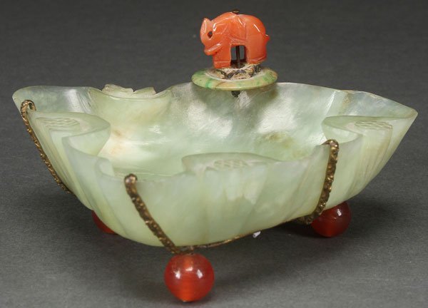 A CHINESE EXPORT CARVED HARDSTONE COUPE: A CHINESE EXPORT CARVED HARDSTONE CARNELIAN AND JADEITE FOOTED DISH, CIRCA 1900. Of leaf form mounted with a carved carnelian elephant on a jadeite bi-disc. The dish raised on carnelian ball feet. Len