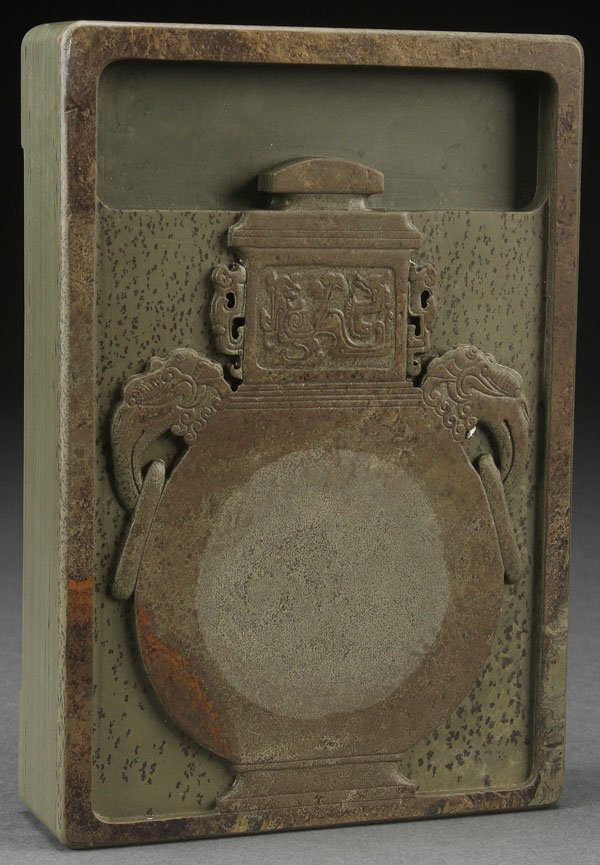A FINE CHINESE CARVED INK STONE.: A FINE CHINESE CARVED INK STONE. Of rectangular form carved in relief with a Ming-style urn in an olive colored stone with dark inclusions, the base with incised seal mark. Length 7.75 inches (19.5 cm