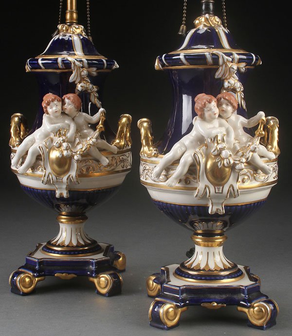 A PAIR OF ROYAL DUX FIGURAL PORCELAIN LAMPS: A PAIR OF ROYAL DUX FIGURAL PORCELAIN LAMPS, FIRST HALF OF THE 20TH CENTURY. In cobalt blue and gilt with putti. Height of porcelain 13.75 inches (35 cm). Overall height 26.5 inches (67 cm).