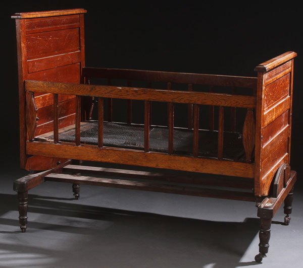 A VICTORIAN ASH PATINATED CRADLE. The paneled hea: A VICTORIAN ASH PATINATED CRADLE. The paneled head and footboard embossed with birds and florals, on four legged stand, which removes for rocking. Length 44 inches (112 cm), width 27.5 inches (70 cm).