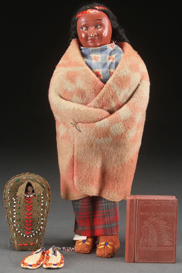 A SKOOKUM INDIAN DOLL, MID 20TH CENTURY: A SKOOKUM INDIAN DOLL, MID 20TH CENTURY. Height 15 inches (38 cm), together with a pipestone carved book form paperweight and a pair of beaded reservation souvenirs.
