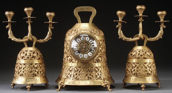 A FRENCH THREE PIECE GILT BRONZE SANCTUARY: A FRENCH THREE PIECE GILT BRONZE SANCTUARY GARNITURE, 20TH CENTURY. Comprising a bell shape clock and matching scroll arm three light candelabra, each with embossed and reticulated designs of musical 