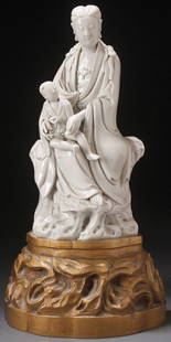 A CHINESE BLANC DE CHINE FIGURE OF KWAN-YIN: A CHINESE BLANC DE CHINE FIGURE OF KWAN-YIN, 17TH/18TH CENTURY. Depicting the seated figure in flowing robes holding a young boy acolyte atop a rockery throne, incised seal and double mark on verso, r