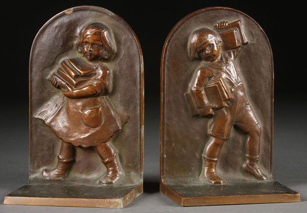 BRONZE BOOKENDS, ZIEGLAR: FRANZ F. ZIEGLAR (GERMAN/AMERICAN FL. 20TH CENTURY). A pair of bronze bookends depicting a young boy and girl carrying books. Signed “F.F. Zieglar Sr.” Copyright 1921. Height 6.75 inches.