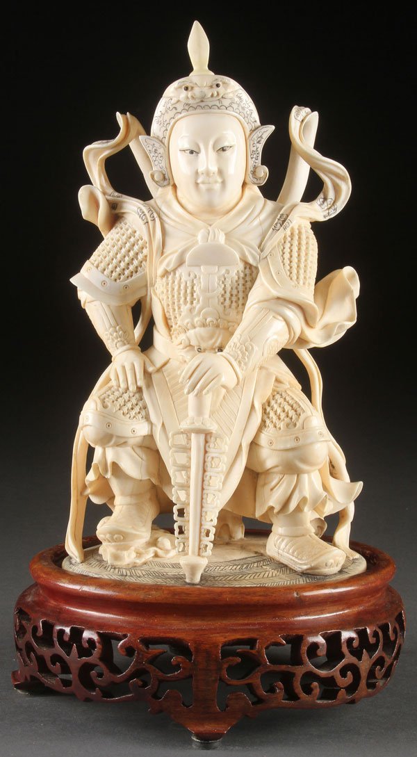 A VERY FINE CHINESE CARVED IVORY WARRIOR GOD: A VERY FINE CHINESE CARVED IVORY WARRIOR GOD FIGURE, CIRCA 1900. Fully carved in the round, depicted wearing a woven armor coat and with scrolled scarves and incised helmet seated on an archaic design