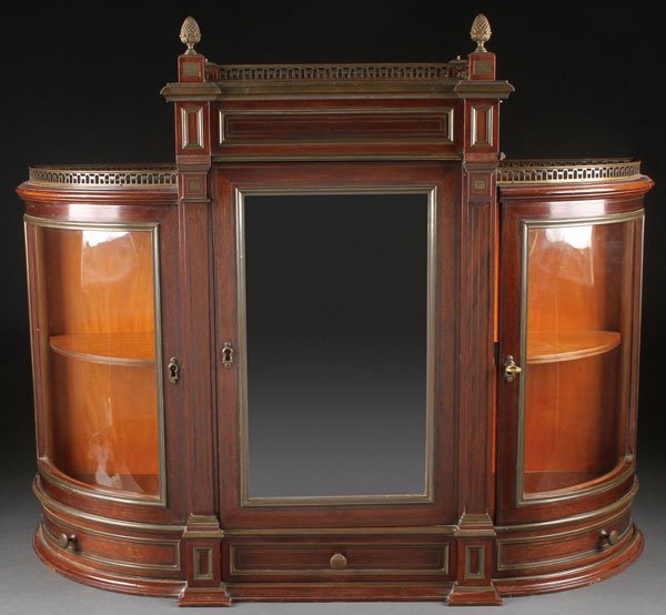 MAHOGANY CURVED GLASS TABLE TOP CURIO DISPLAY: A SMALL MAHOGANY CURVED GLASS AND BRONZE MOUNTED TABLE TOP VITRINE, 19TH CENTURY. The mirrored beveled glass door opening to reveal a satin wood interior and flanked by two curved glass displays below