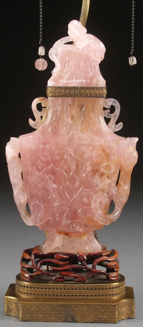 A CHINESE CARVED ROSE QUARTZ URN AS A LAMP: A CHINESE CARVED ROSE QUARTZ URN AS A LAMP, EARLY 20TH CENTURY. The hollowed urn panels carved in relief with scrolling foliage flanked by two figural carved and pierced dragonettes below archaic styl