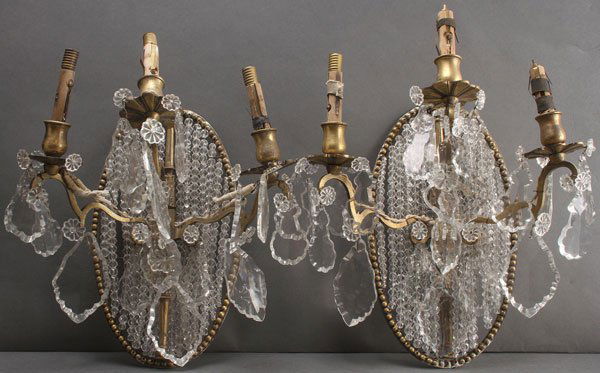A PAIR OF FRENCH GILT BRONZE AND CUT CRYSTAL WALL: A PAIR OF FRENCH GILT BRONZE AND CUT CRYSTAL WALL SCONCES, CIRCA 1900. Each comprised of a beaded oval medallion suspending chains of cut crystals and mounted with three Louis XV style candle arm brac