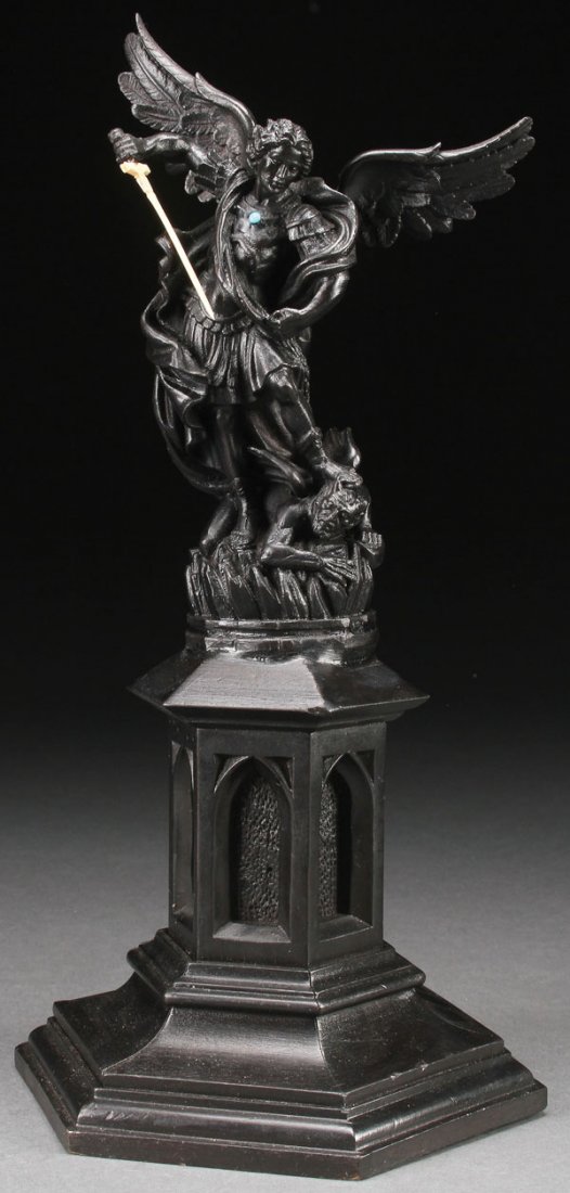 CARVED WOOD FIGURE OF SAINT MICHAEL: A CARVED EBONIZED WOOD FIGURE OF ST. MICHAEL DEFEATING SATAN. Resting on a hexagonal, stepped base from which rises a Gothic column, upon which rests the finely carved wood figure rendered in full rou