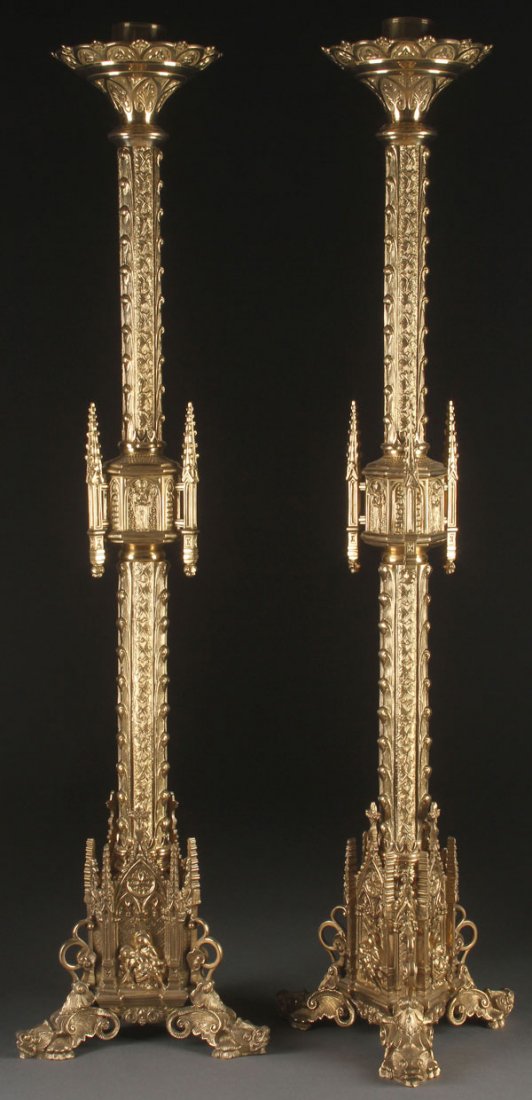 GIGANTIC GILT BRONZE GOTHIC CANDLE STANDS: A PAIR OF LARGE AND IMPRESSIVE GILT BRONZE NEO GOTHIC CANDLE STANDS, FIRST HALF 20TH CENTURY. Each resting on three ornately sculpted raised dragon head feet, the three sided bases with Gothic arched 
