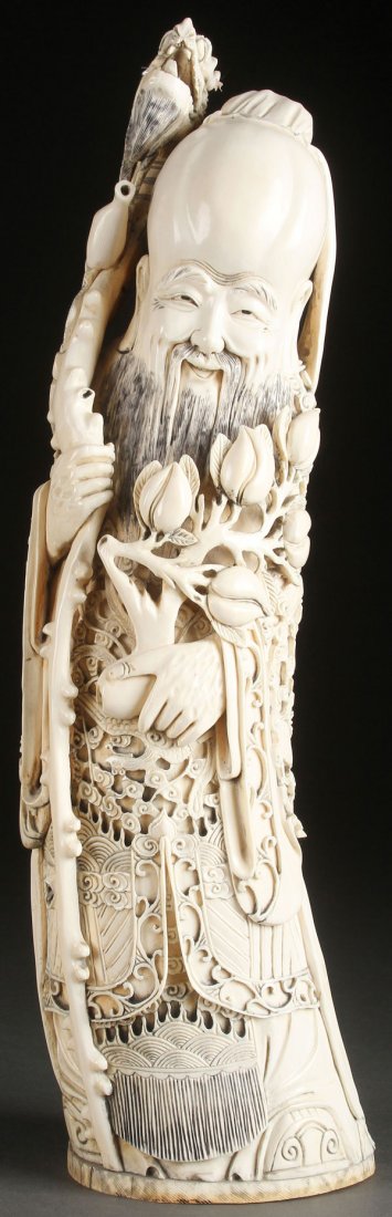 CHINESE CARVED IVORY TUSK, CIRCA 1920: A LARGE CHINESE CARVED IVORY TUSK OF THE GOD OF LONGEVITY, CIRCA 1920. Carved in deep relief with good detail and form depicting a standing figure wearing a dragon’s robe and holding a dragon headed