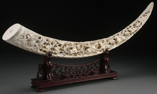 CHINESE SCENIC CARVED IVORY TUSK, CIRCA 1950: A LARGE CHINESE SCENIC CARVED IVORY TUSK, CIRCA 1950. Fully carved in the round and pierced with a scenic depiction of battling warlords on horseback below pine trees and terminating with a dragon on 
