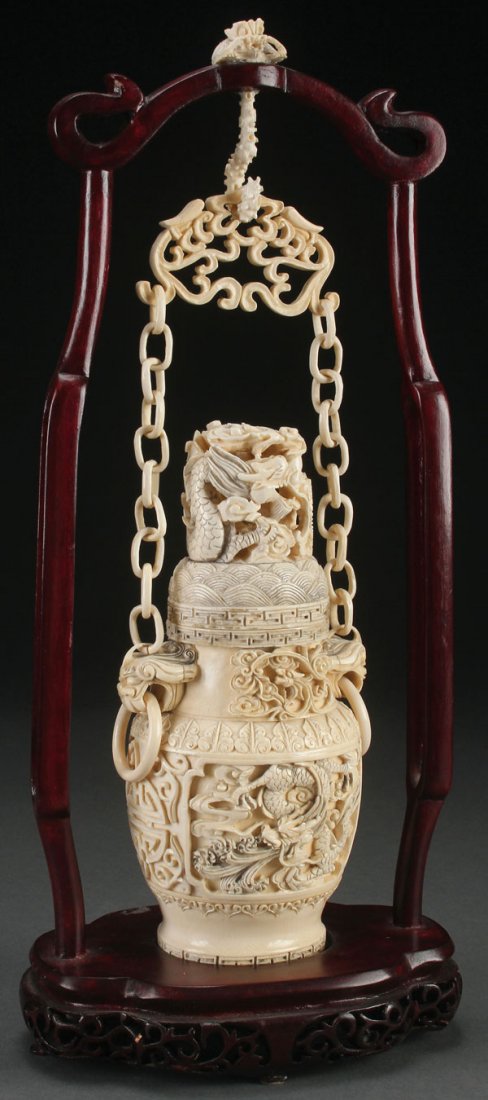 CHINESE CARVED IVORY HANGING LIDDED URN, C 1910: A FINE CHINESE CARVED IVORY HANGING LIDDED URN, CIRCA 1910. The ovoid form urn carved in fine relief and good detail with scenic panels of dragons below figural mythical beast handles suspending loos