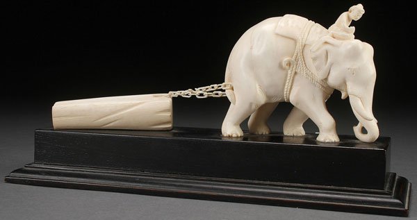 A FINE SINO-TIBETAN CARVED IVORY FIGURAL GROUP: A FINE SINO-TIBETAN CARVED IVORY FIGURAL GROUP, CIRCA 1950. Sculpted as a domesticated working elephant dragging a log bound with a carved ivory chain mounted on an ebony wood plinth. Total length 11.